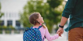 Young girl with polka dot backpack holding adult's hand outdoors