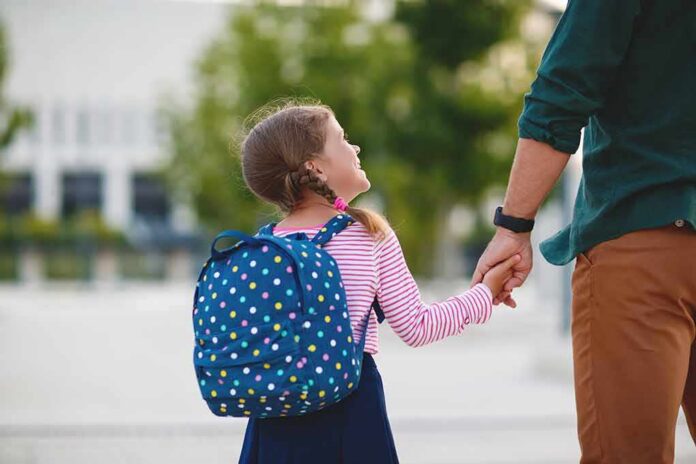 Young girl with polka dot backpack holding adult's hand outdoors