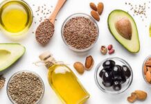 Assorted healthy fats with avocados, nuts, seeds, olives, and oils on a white background