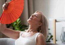 Drug-Free Menopause Breakthrough Stuns Woman fanning herself with an orange hand fan