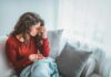 Woman sitting on couch holding pills and rubbing her forehead