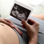Pregnant person holding an ultrasound photo over their belly
