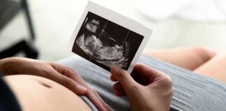 Pregnant person holding an ultrasound photo over their belly