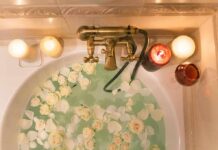 Bathtub filled with water and white roses under candles