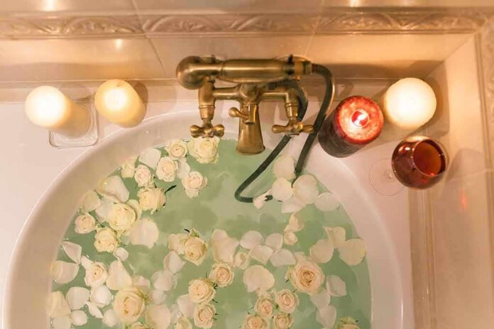 Bathtub filled with water and white roses under candles
