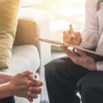Doctor with clipboard talking to patient on a sofa